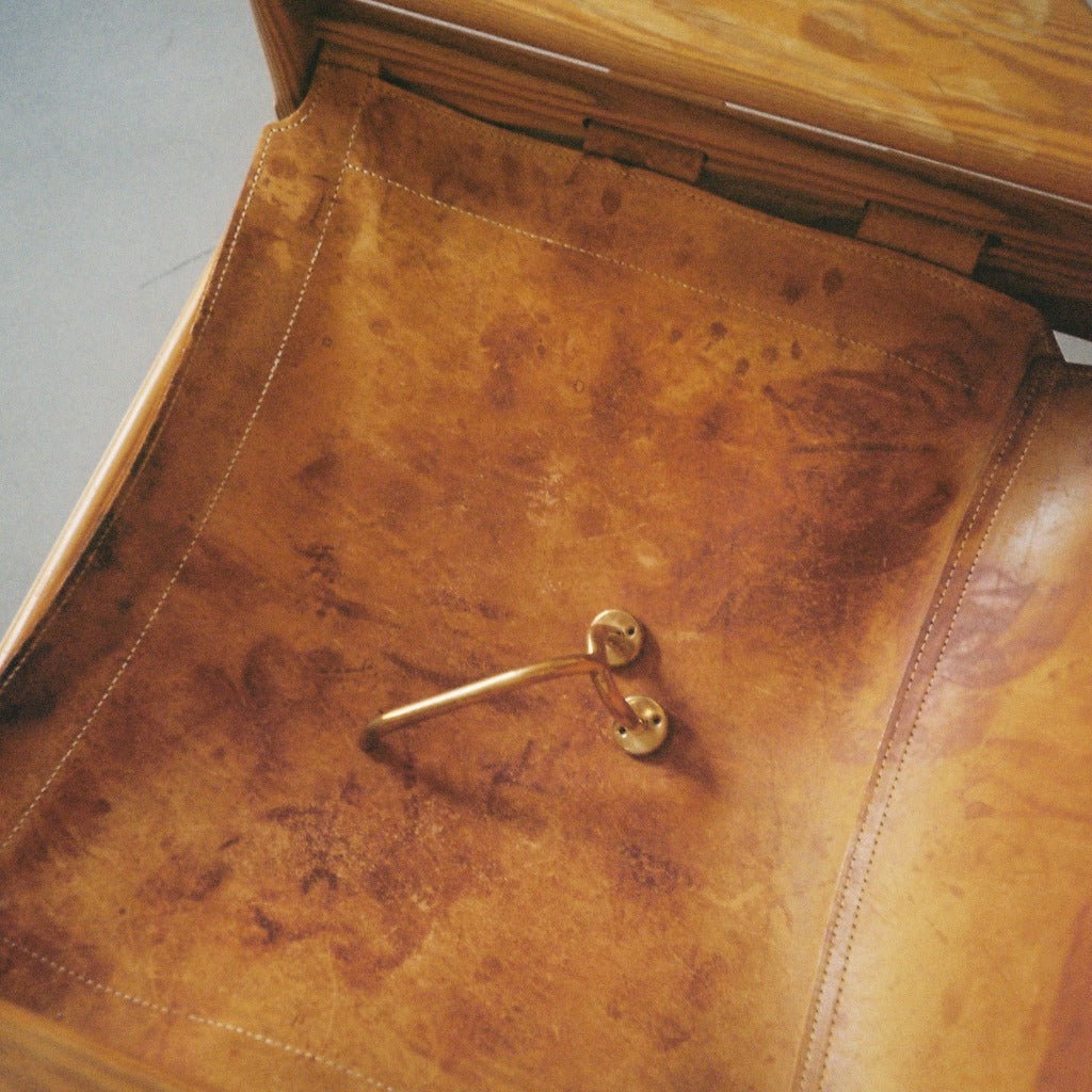 Brass Maha Alavi Fauna toilet paper holder on a tan leather surface.