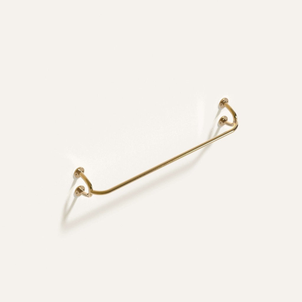 Fauna Towel Bar in polished brass installed on a white wall showcasing it's gentle curves and clean lines.