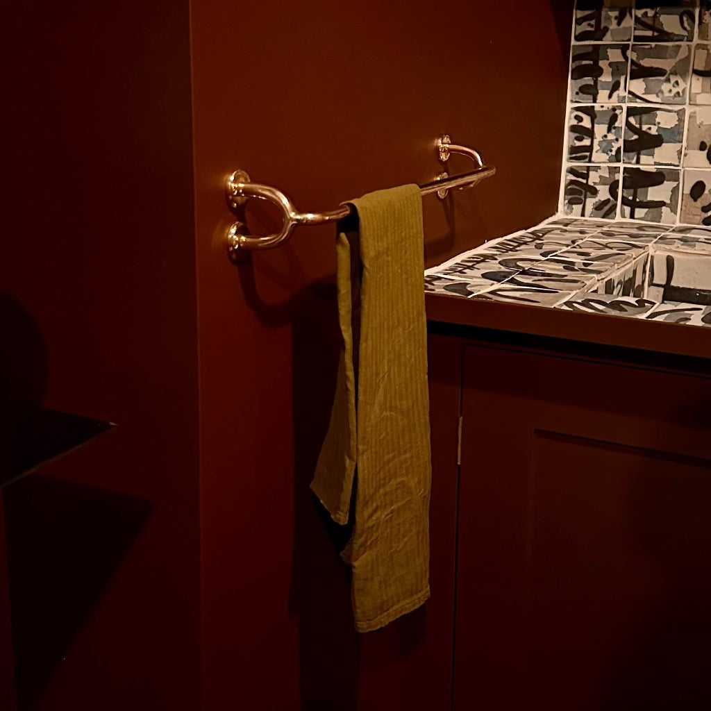 Brass Maha Alavi Fauna towel bar with a yellow towel in a dark bathroom.