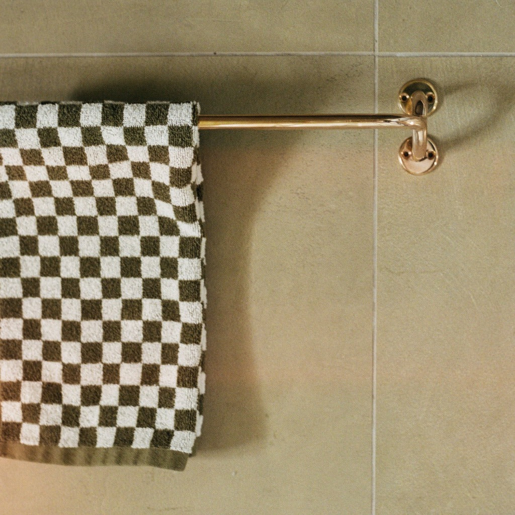 Brass Maha Alavi Fauna towel bar with a checkered towel on tile.