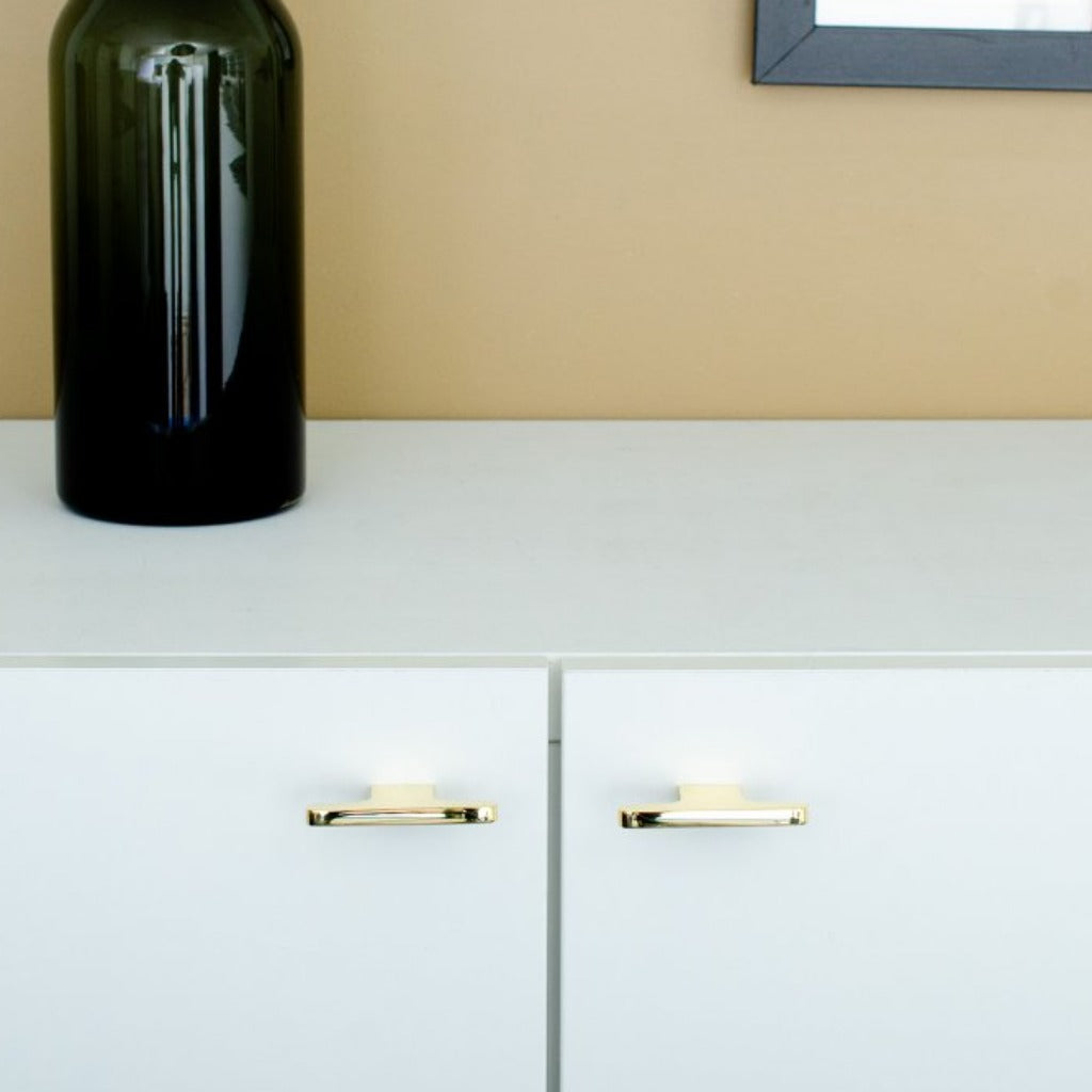 T shaped knobs in polished brass mounted on a white cabinet