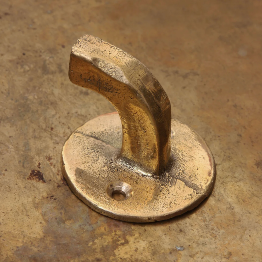 Hand-cast solid brass Forme No. 8 hook with a curved, architectural profile and a textured, matte finish on a brass surface.
