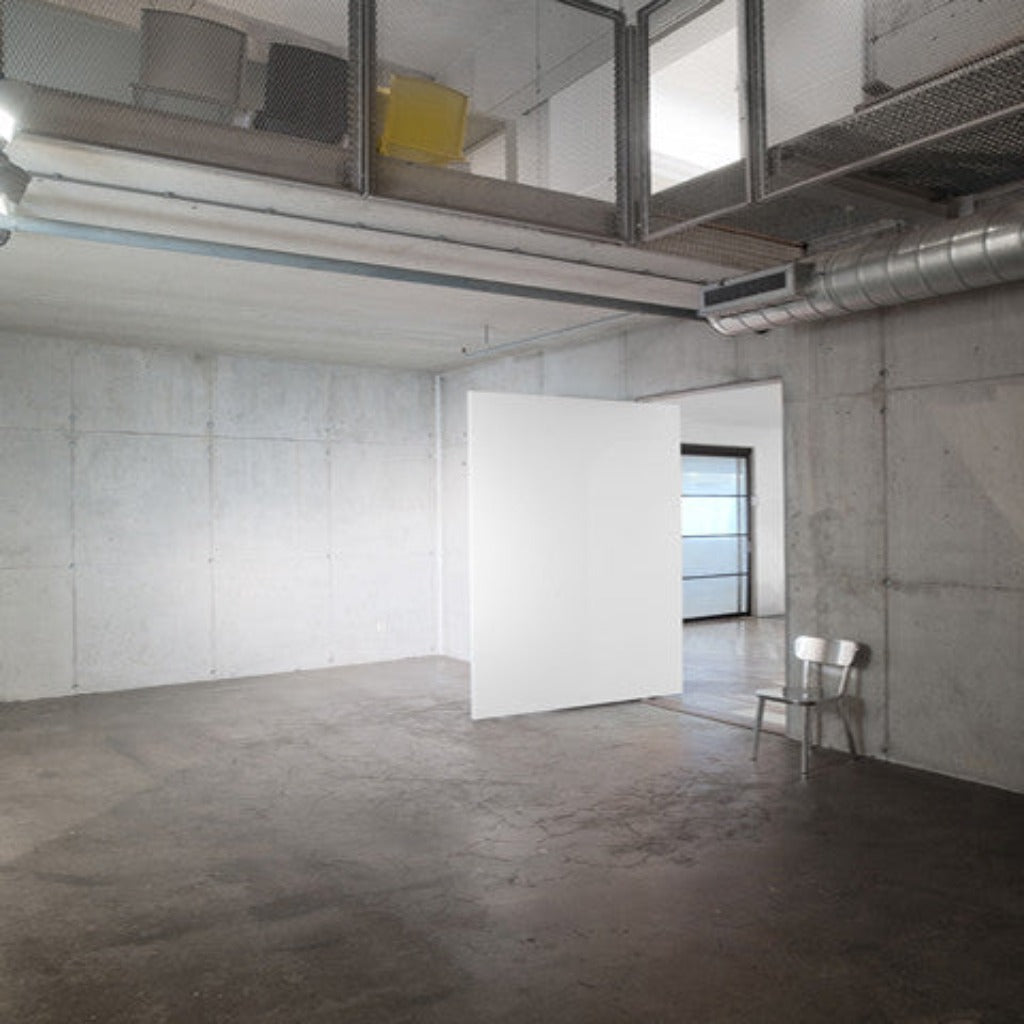 An empty room with a white wall and a FritsJurgens Pivot Door Hinge System 3 chair.