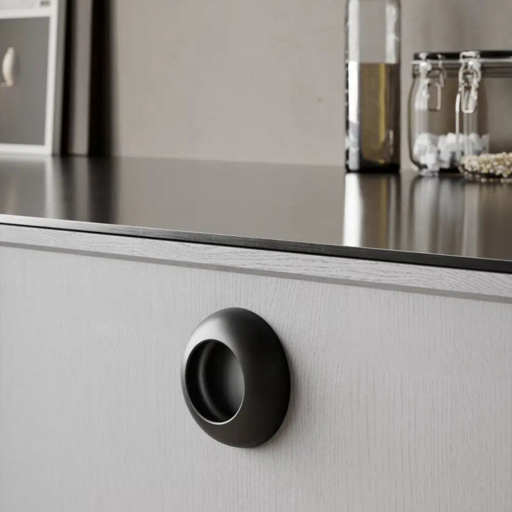 Black cup-style cabinet knob mounted on white drawer