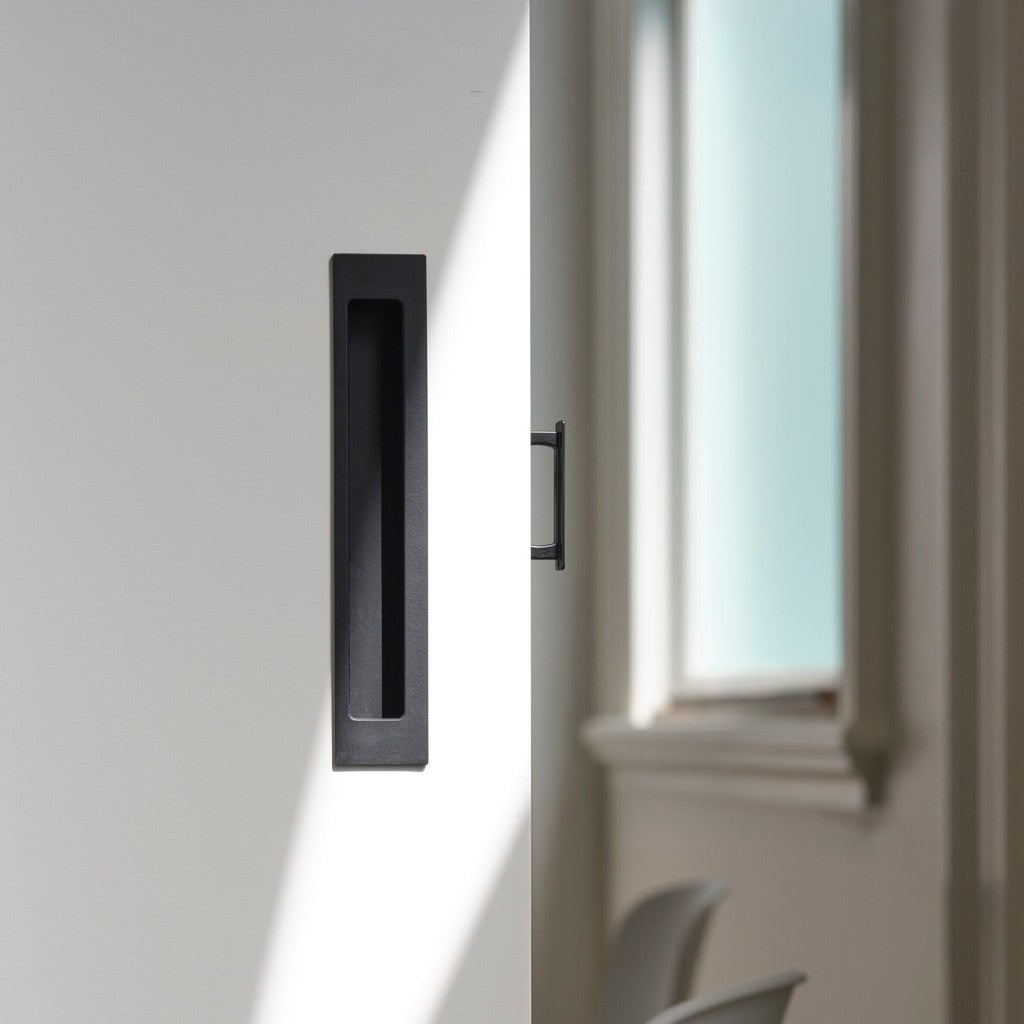 Matte black HB 677 bi-fold flush pull recessed into a pivot door beside a window.