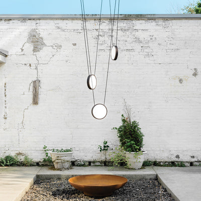 A Highwire Pendant by Anony hanging in front of a white brick wall.