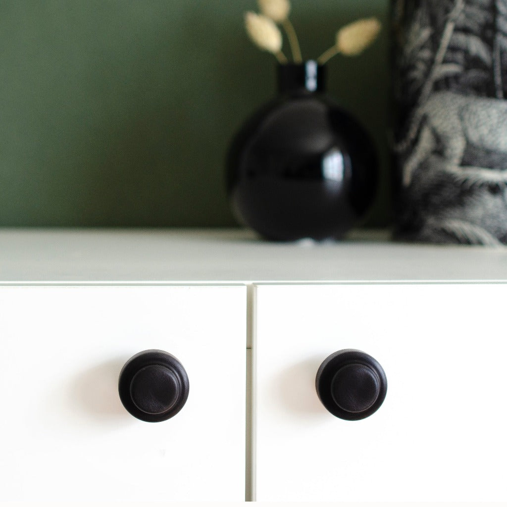 a white dresser with two black Baccman Berglund Hip Knobs/Hooks on top of it.