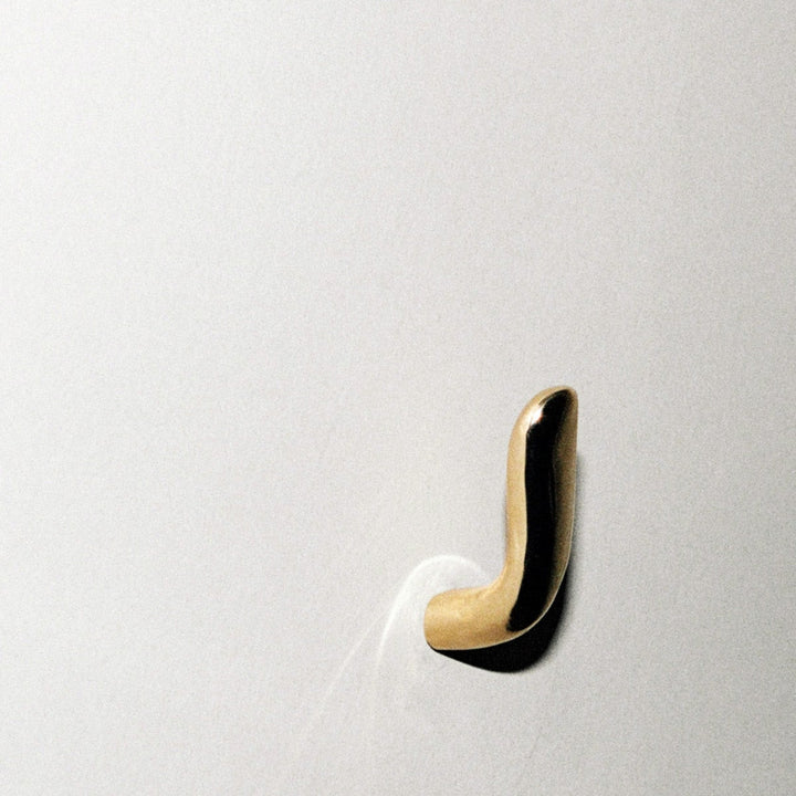 Softly curved J shaped hook in polished brass, mounted to wall.