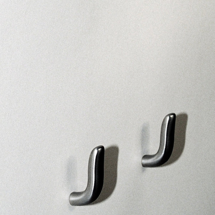 Two softly curved J shaped hooks in satin nickel, mounted to wall.