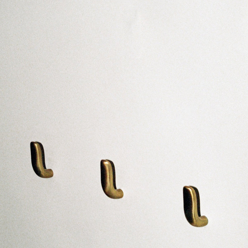 Three softly curved J shaped hooks in amber brass, mounted to wall.