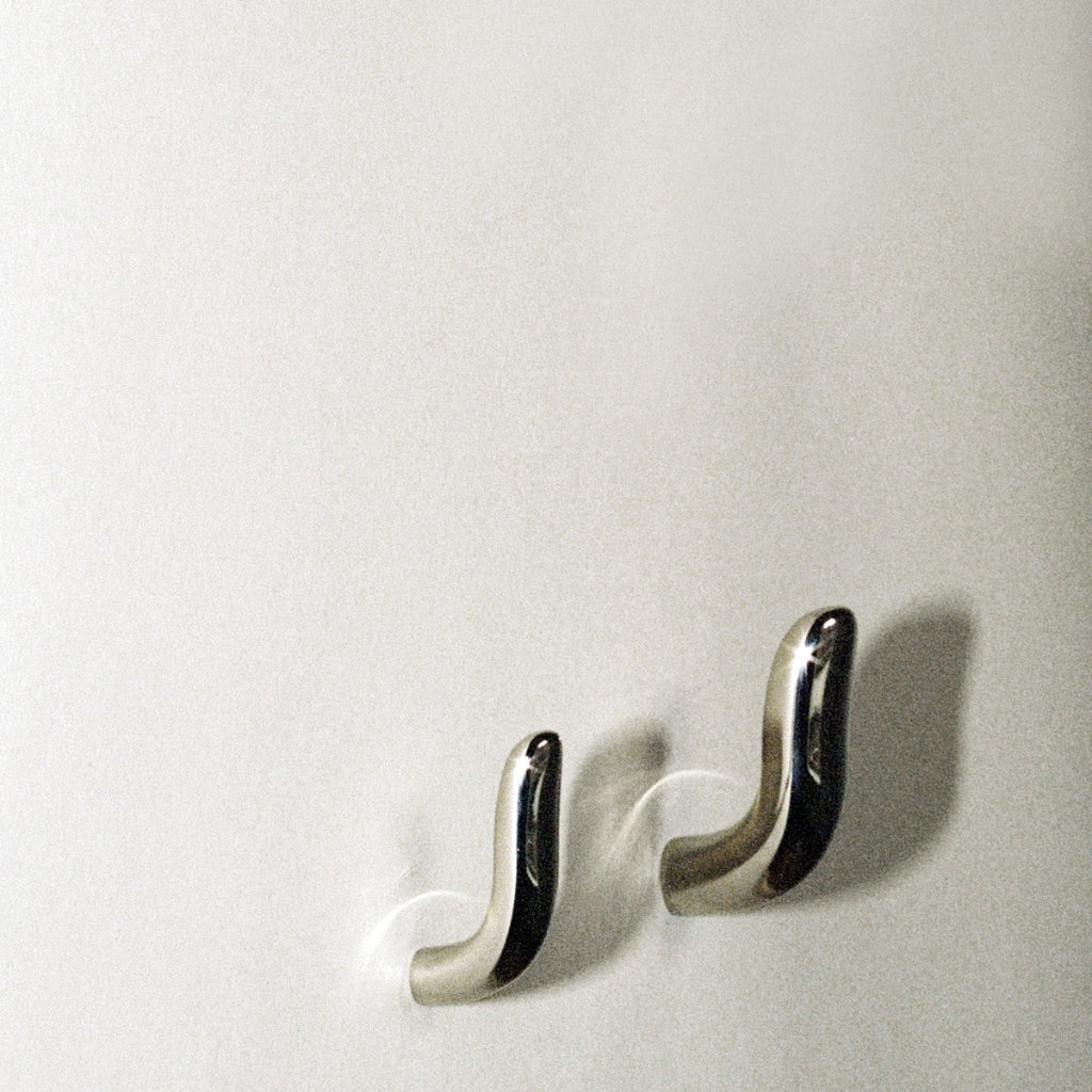 Two softly curved J shaped hooks in polished nickel, mounted to wall.