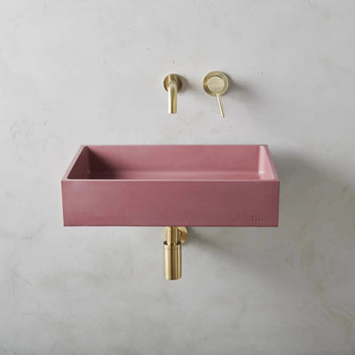 A mudd. concrete Jeker Basin Affix with a gold faucet and a pink sink.