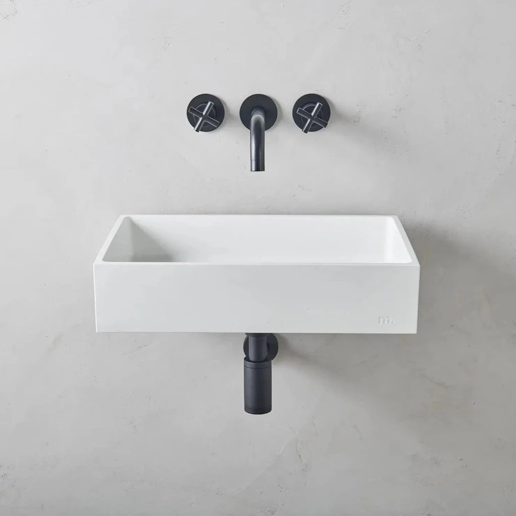 A mudd. concrete Jeker Basin Affix sink with two black faucets on the wall.