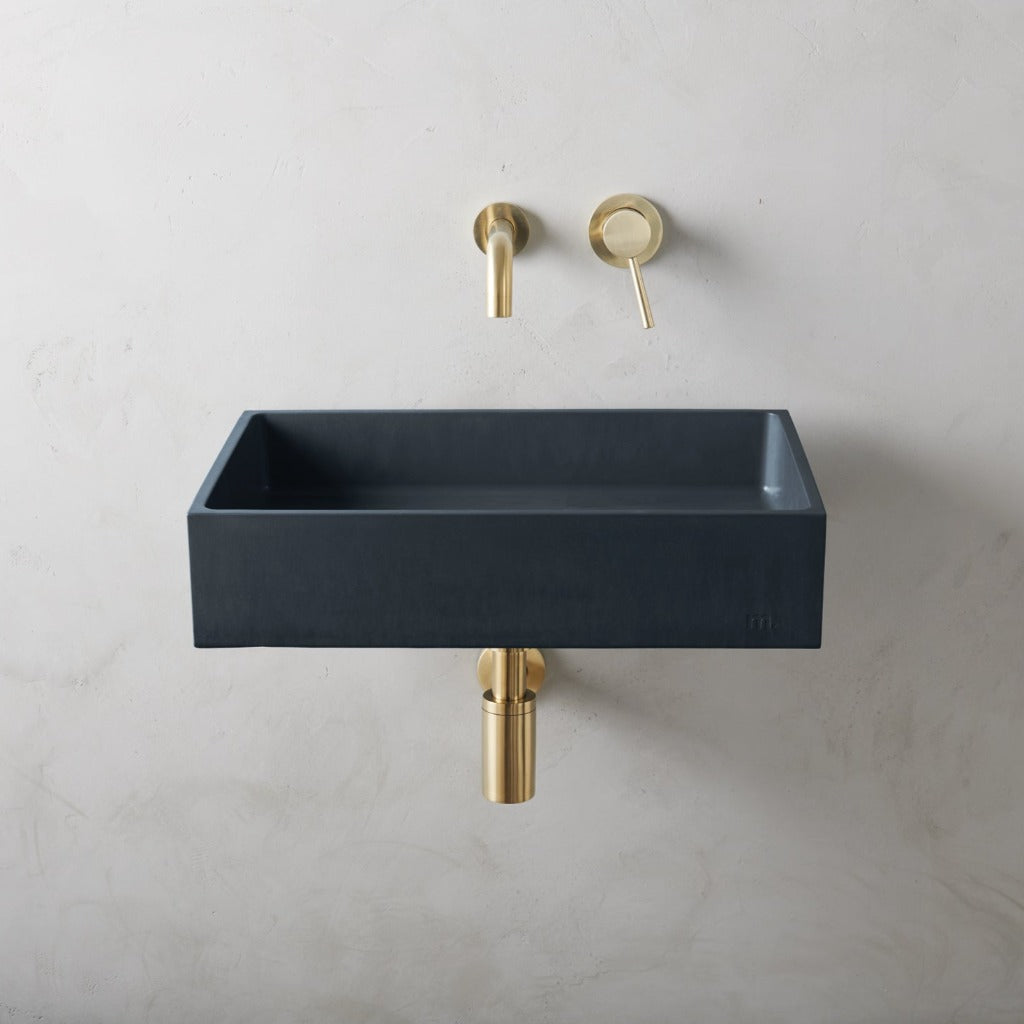 a mudd. concrete Jeker Basin Affix with a gold faucet and a black sink.