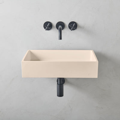 A mudd. concrete Jeker Basin Affix with two black faucets on the wall.