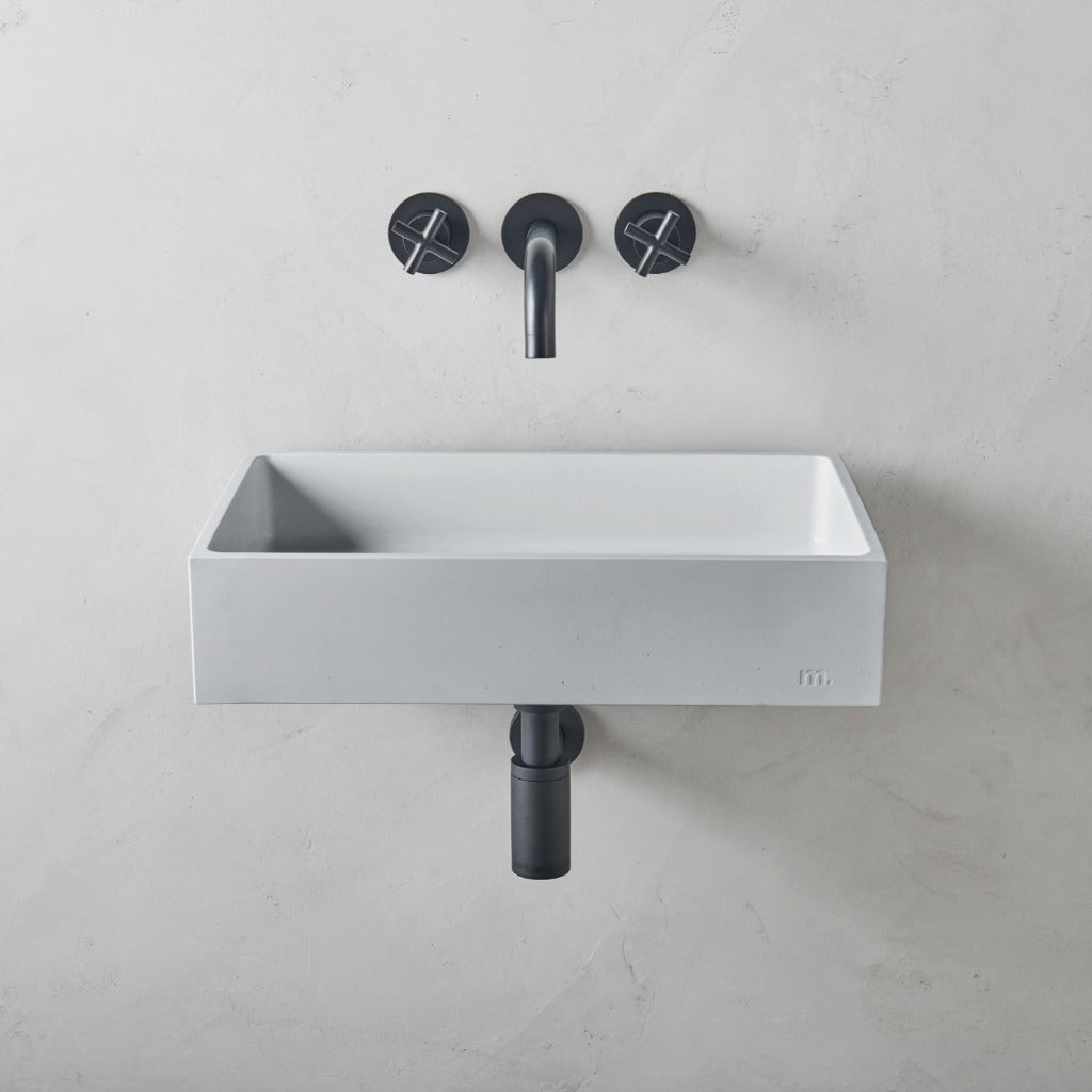 A mudd. concrete Jeker Basin Affix with two black faucets on the wall.