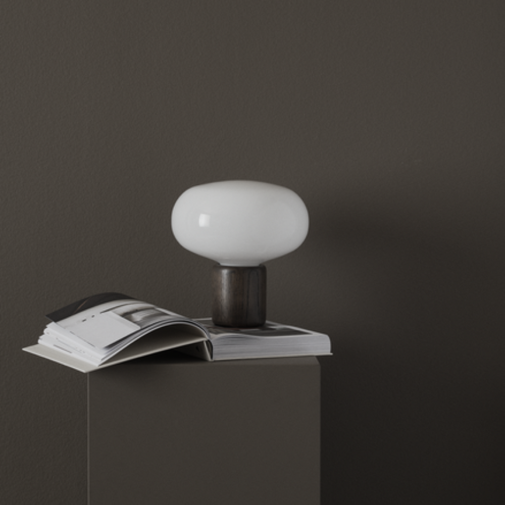 A table lamp with a dark oak base and a rounded opal glass top, placed on a book