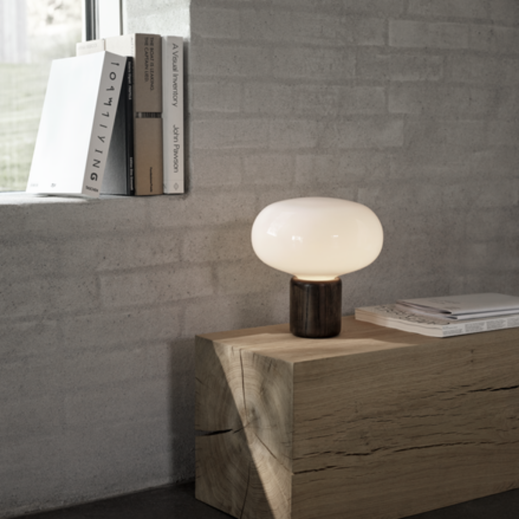 A table lamp with a dark oak base and a rounded opal glass top, placed on a wooden table