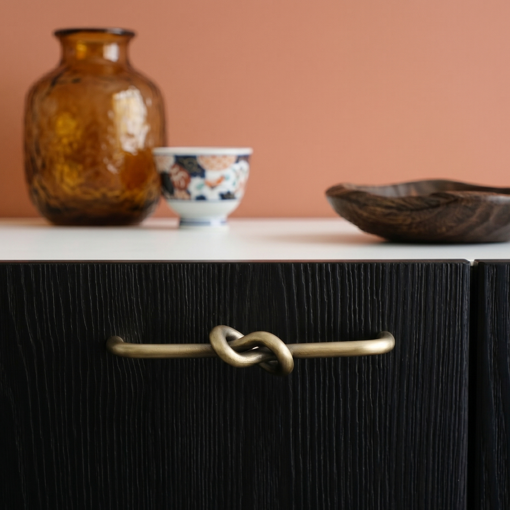 Black cabinet with a knotted handle, brown vase, and bowl on a white surface against a peach wall.