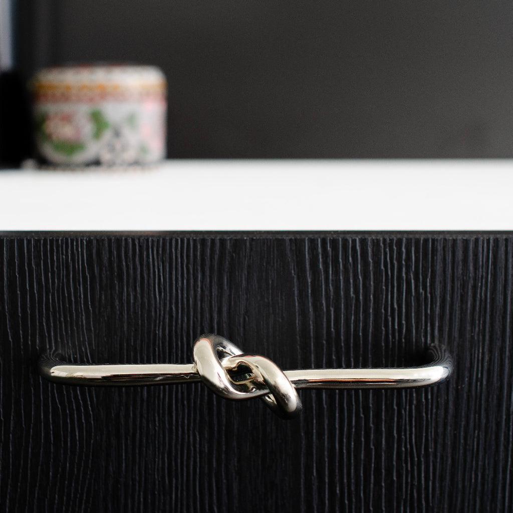 Silver knot-shaped cabinet handle on a black wooden kitchen cabinet with a blurred background