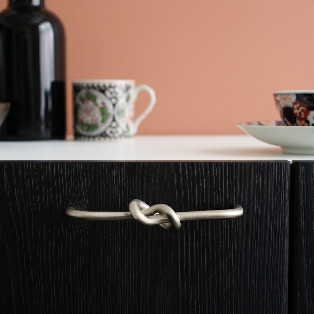 Black cabinet with a unique handle design, featuring a cup and saucer in the background.