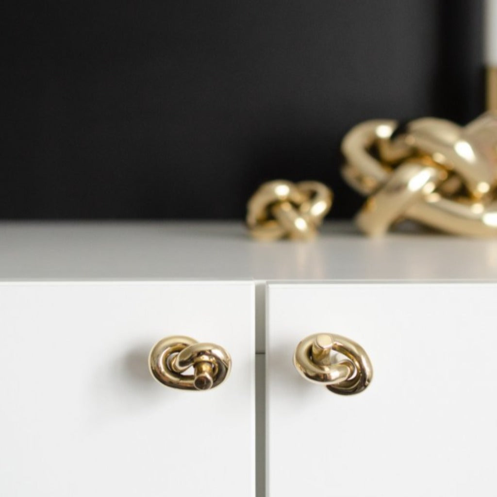 Baccman Berglund Brass Knot Knob installed on white cabinet with brass accessories on display