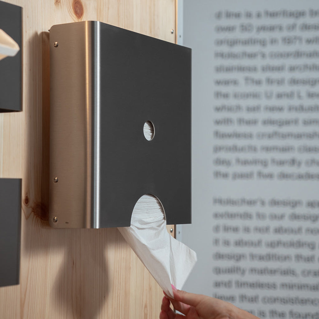 Bronze d line Knud paper towel dispenser in use on a wall.