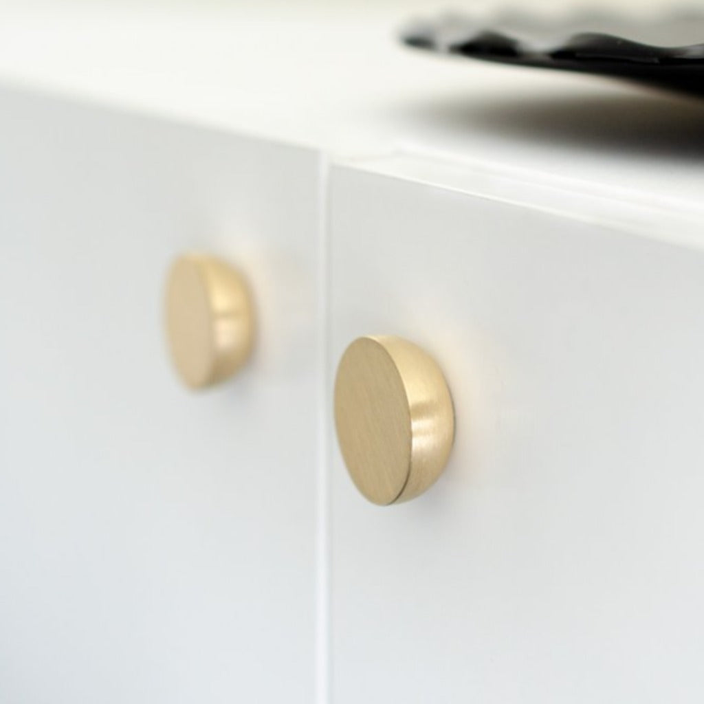 Round knob in brushed brass by Baccman Berglund mounted on white cabinet