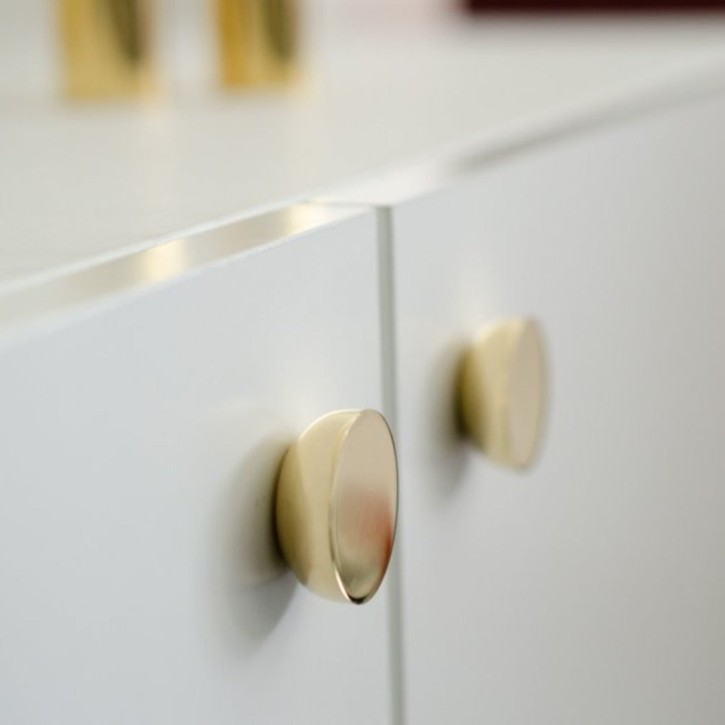 Round knob in polished brass by Baccman Berglund mounted on white cabinet