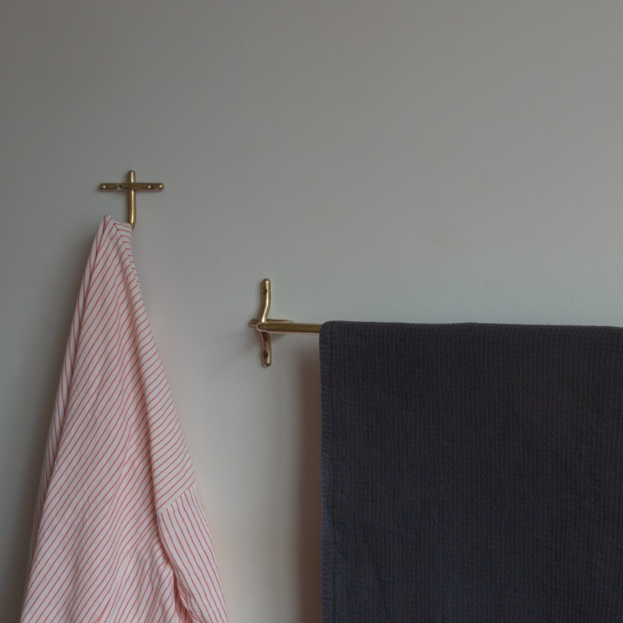 Brass towel rack  and bath hook with pink and dark towels on a plain wall