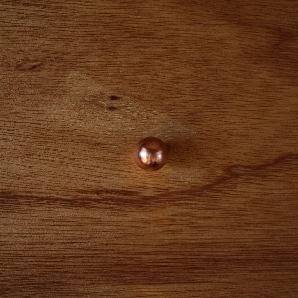 Copper Maha Alavi LUA knob, a rounded ball, on a wood drawer.
