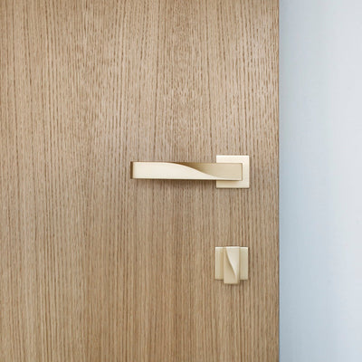 Elegant brass lever handle with square rose and thumb turn on light wood door. Beautifully and functionally designed.