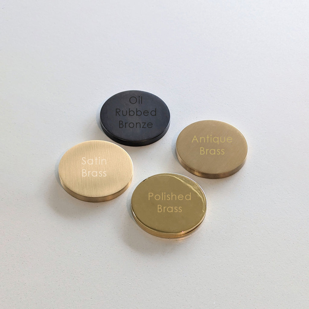 Three Maison Vervloet Finish Sample brass and black colored buttons on a white surface.