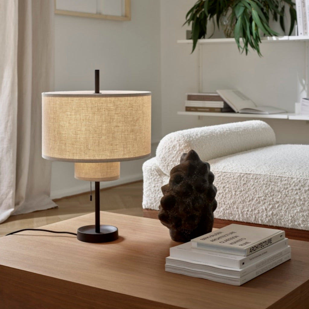 A round, tiered table lamp with a thin, black base, placed on a wooden coffee table