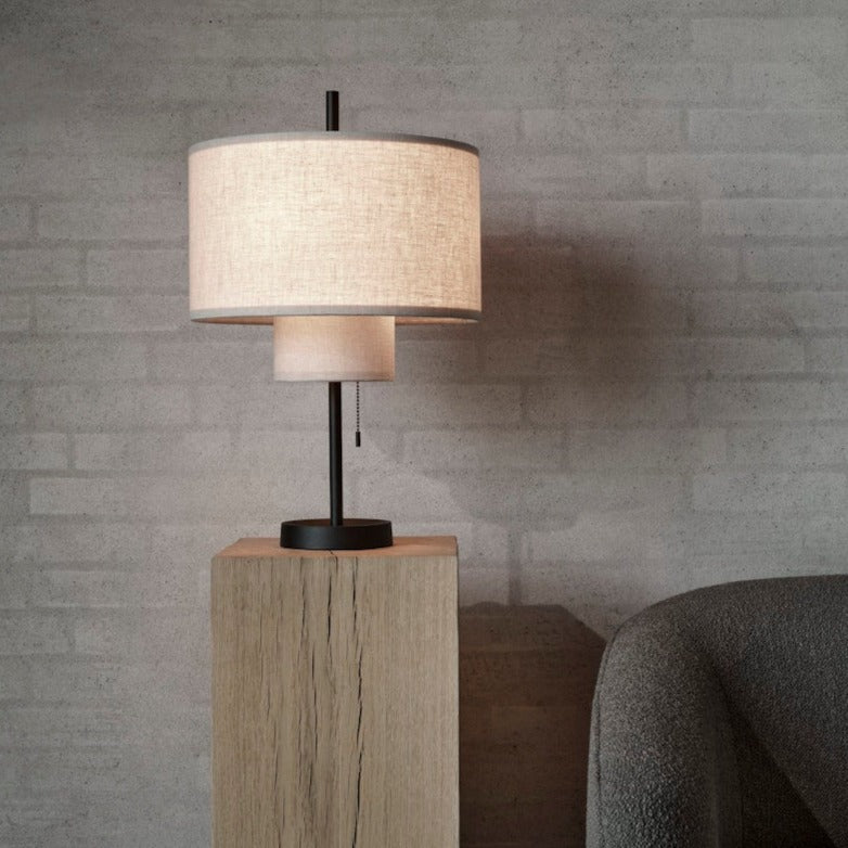 A round, tiered table lamp with a thin, black base, placed on a wooden stand