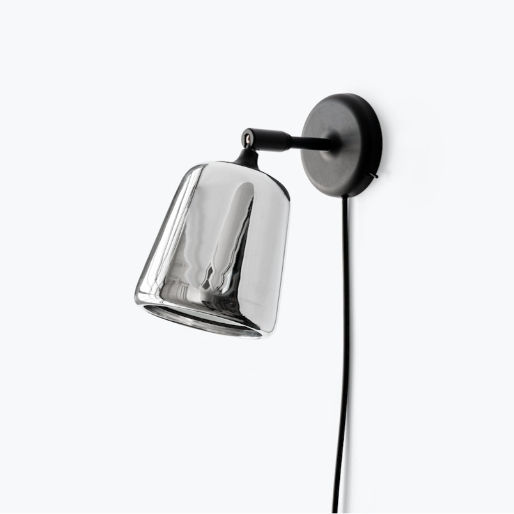 Minimalist wall lamp with a reflective glass shade and black pivoting arm mounted on a plain white background.