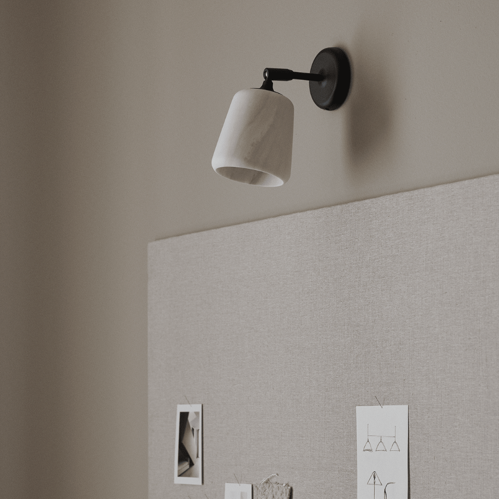 Minimalist wall lamp with a white marble shade and black pivoting arm mounted on a neutral beige wall.