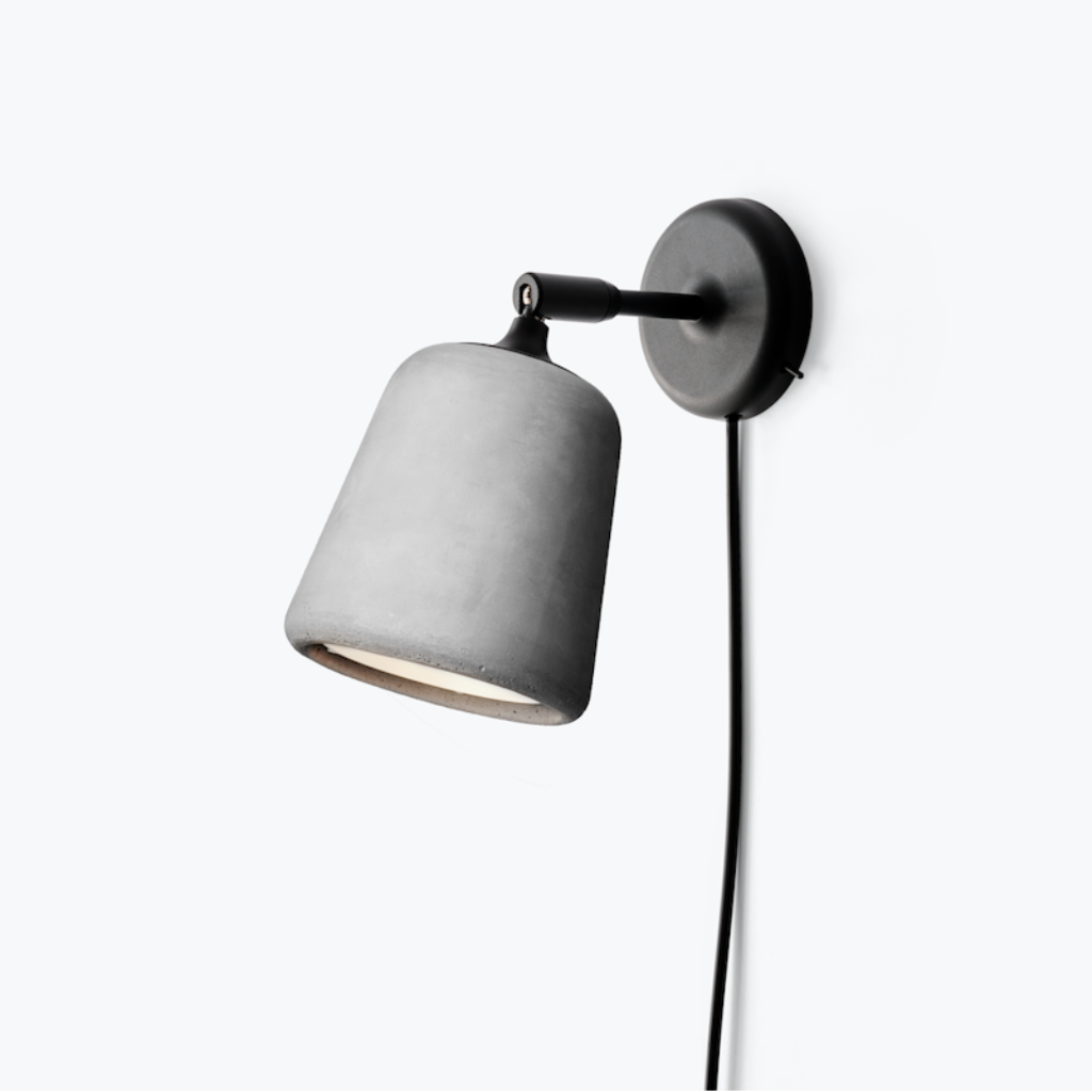 Minimalist wall lamp with a grey concrete shade and black pivoting arm mounted on a plain white wall.