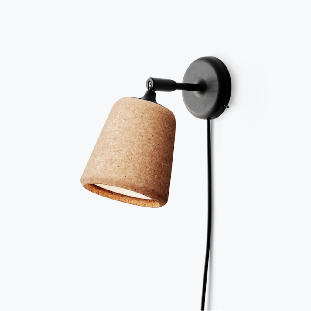 Minimalist wall lamp with a textured cork shade and black metal pivoting arm mounted on a plain white wall.