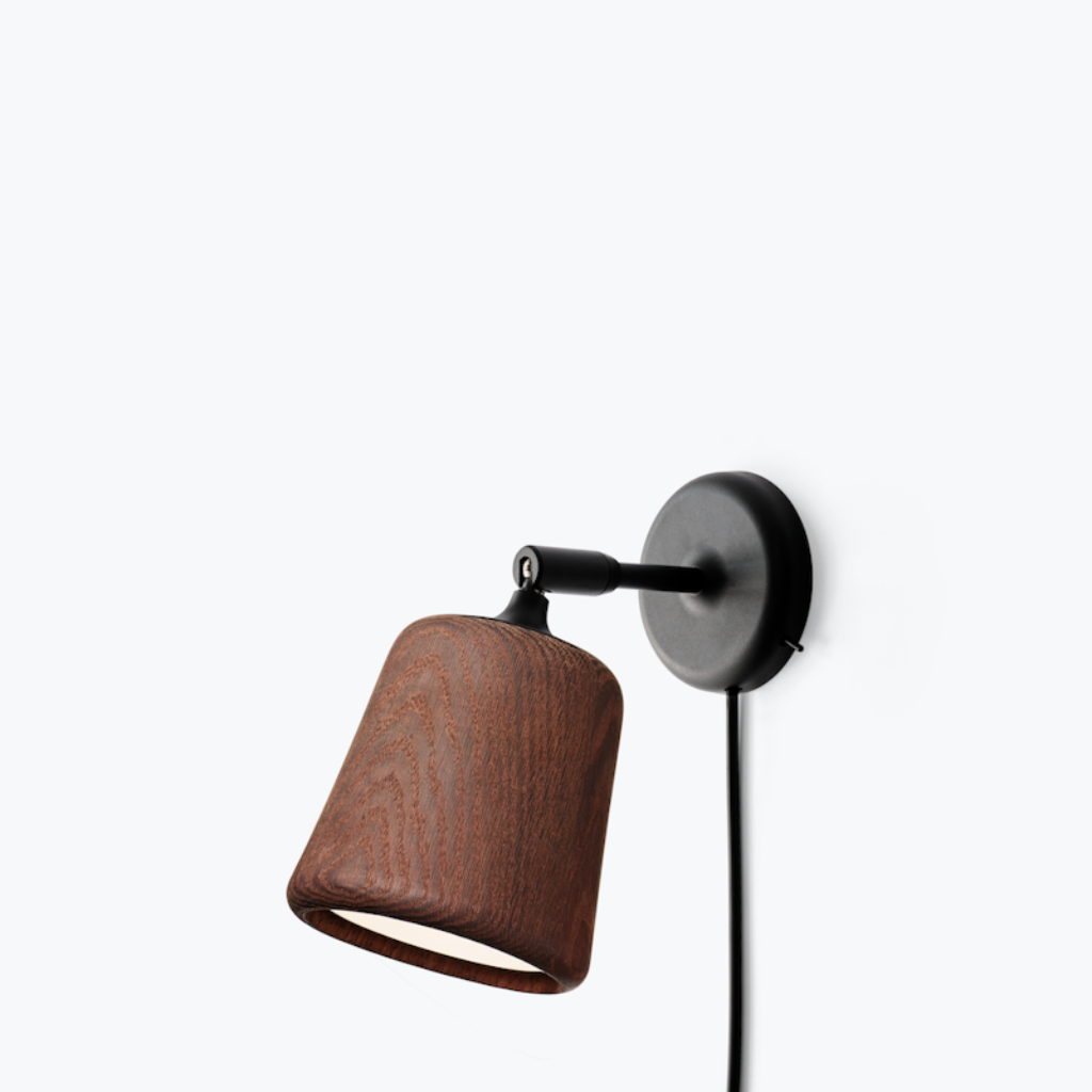 Minimalist wall lamp with a dark wood shade and black pivoting arm on a white wall.