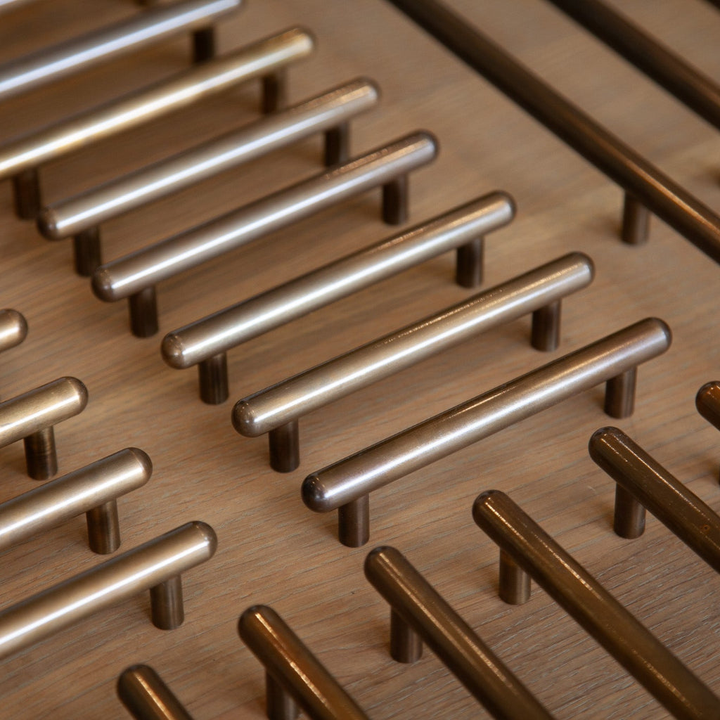 Chapman & Bose metal bar pulls in a row on wood, in mixed steel and bronze finishes.