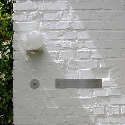A white brick wall with a Serafini Modern Circle Doorbell on it.