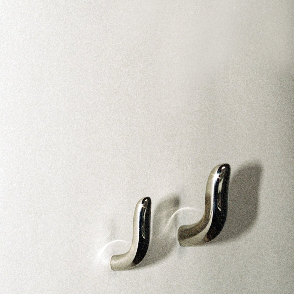 Two softly curved J shaped hooks in polished nickel, mounted to wall.
