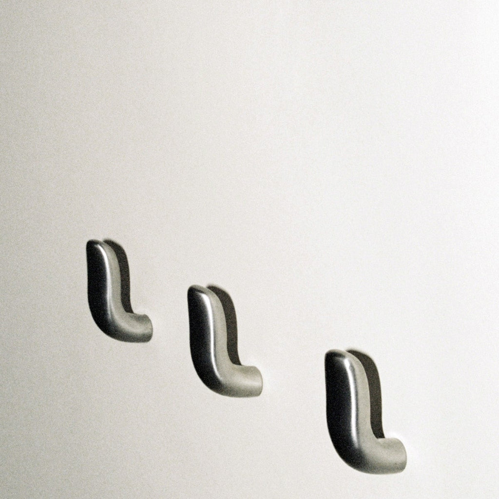 Three softly curved J shaped hooks in satin nickel, mounted to wall.