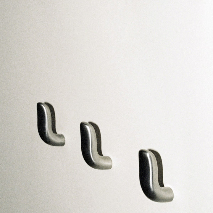 Three softly curved J shaped hooks in satin nickel, mounted to wall.