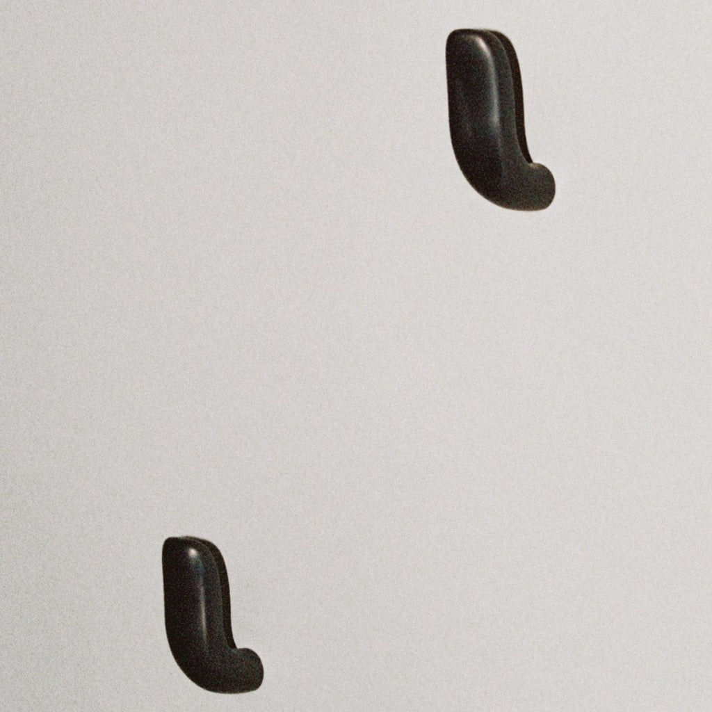 Two softly curved J shaped hooks in dark brass, mounted to wall.