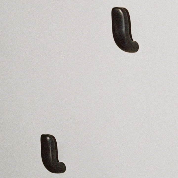 Two softly curved J shaped hooks in dark brass, mounted to wall.