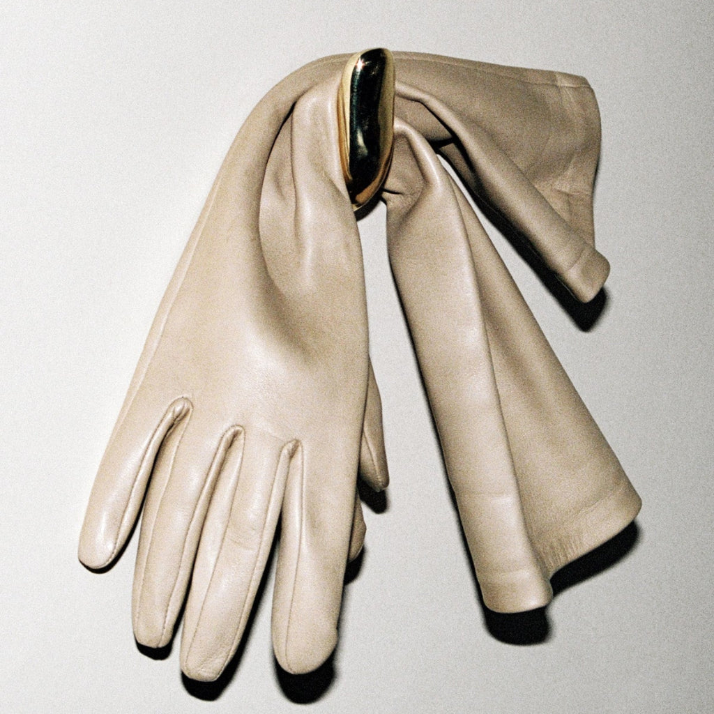Softly curved J shaped hook in polished brass, with cream coloured gloves hanging off of it.