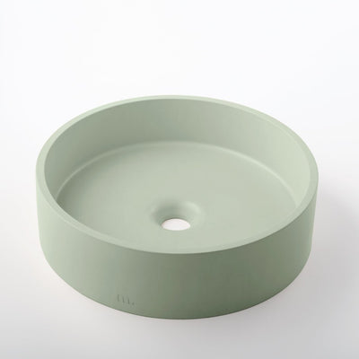 A round green Odet Basin LG sink on a white mudd. concrete surface.