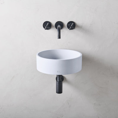 A mudd. concrete Odet Basin SM Affix with two black faucets on the wall.